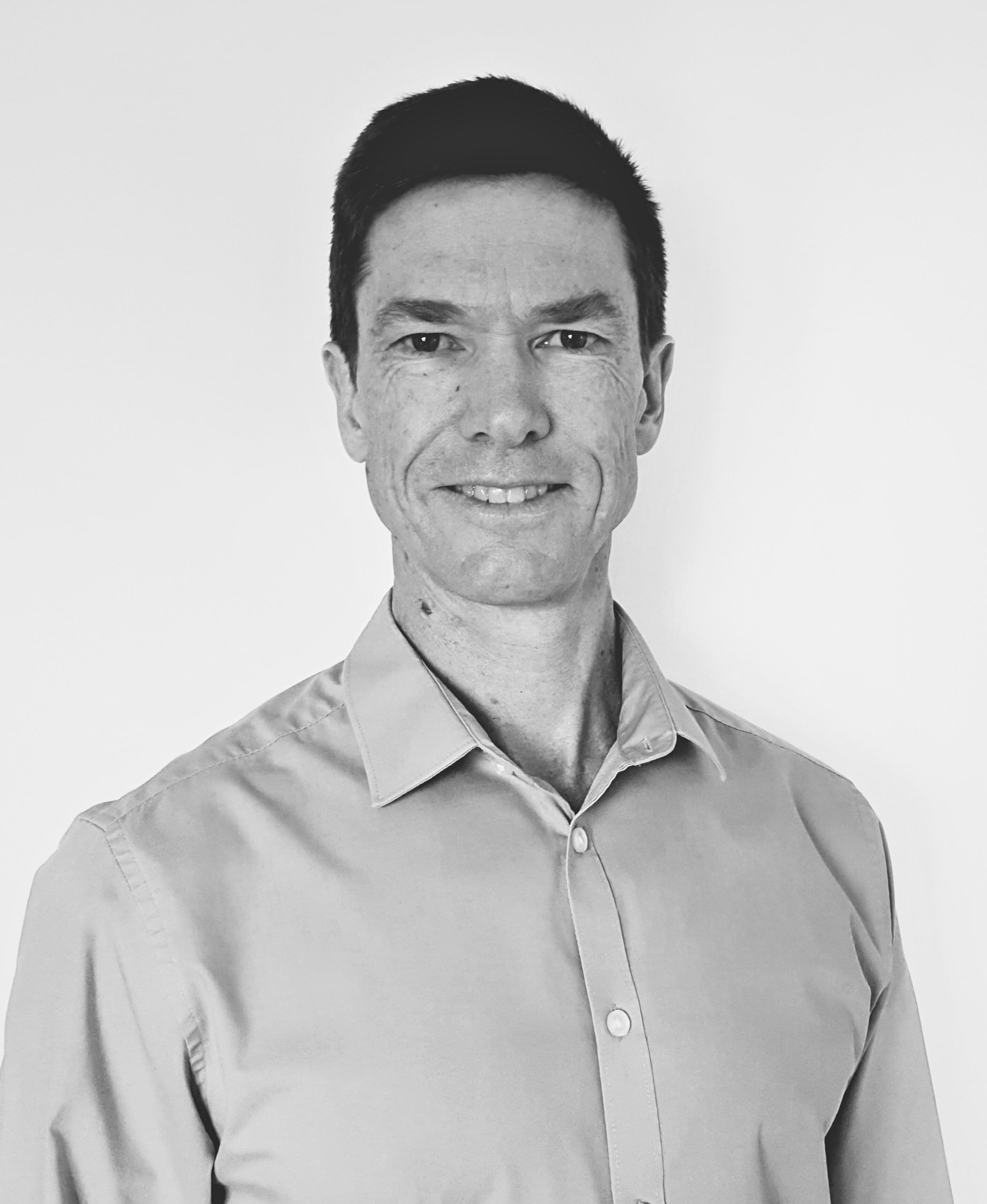 Jeremy Wakeford com camisa está diante de uma parede branca, a sorrir para a câmara