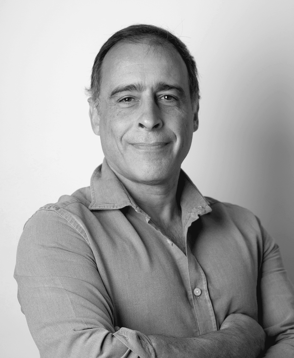 Jose Maria Mascarenhas está diante de uma parede branca, com camisa, a sorrir ligeiramente para a câmara