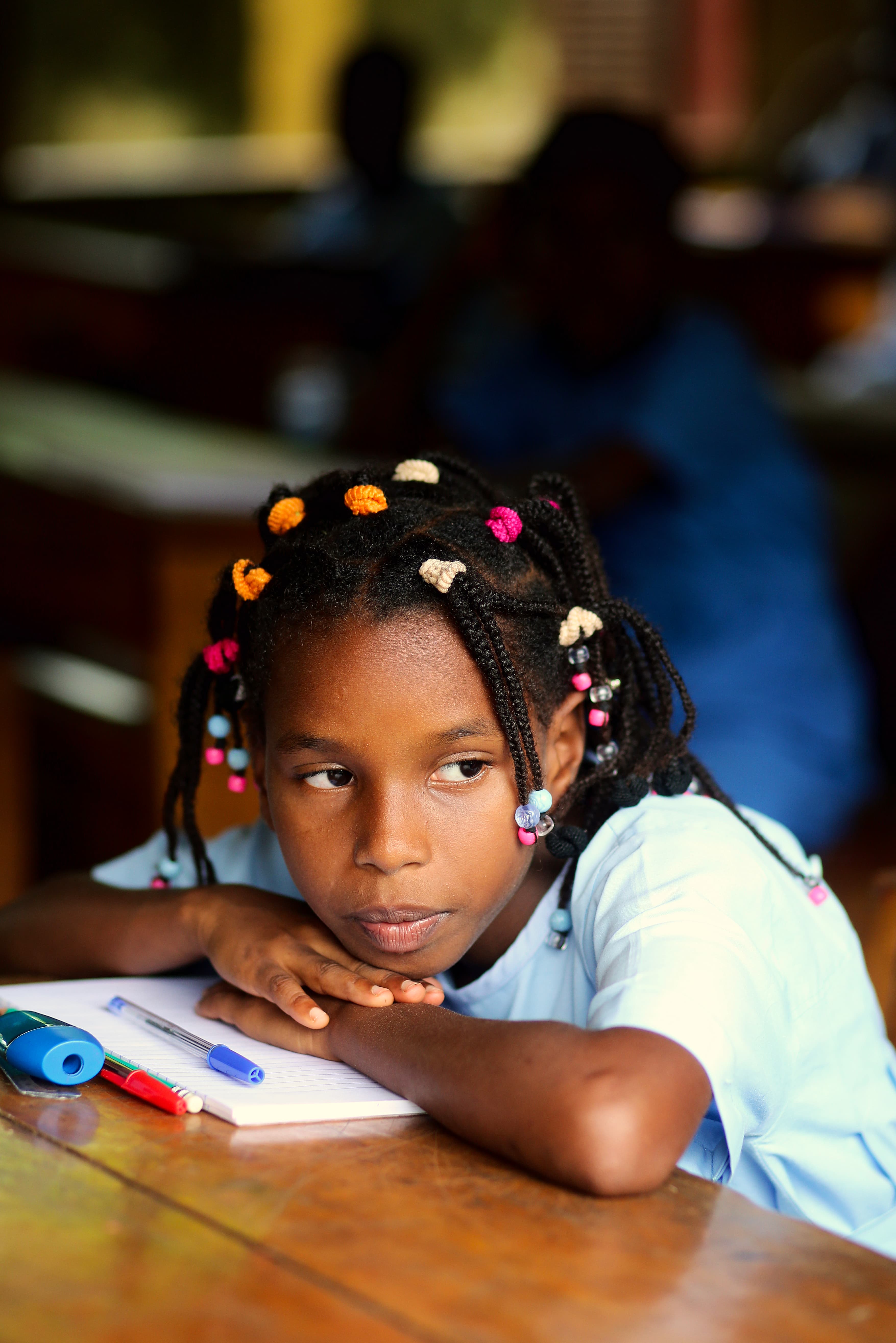 Girl with colourful beads in her hair sits hunched over her schoolbook