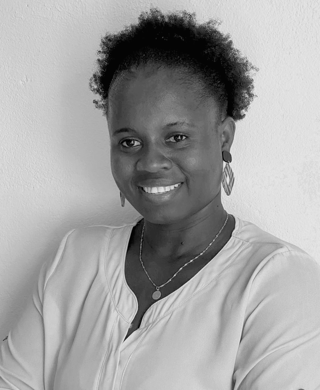 Retrato de Emelinda Mendes com blusa branca, diante de uma parede branca, a sorrir para a câmara