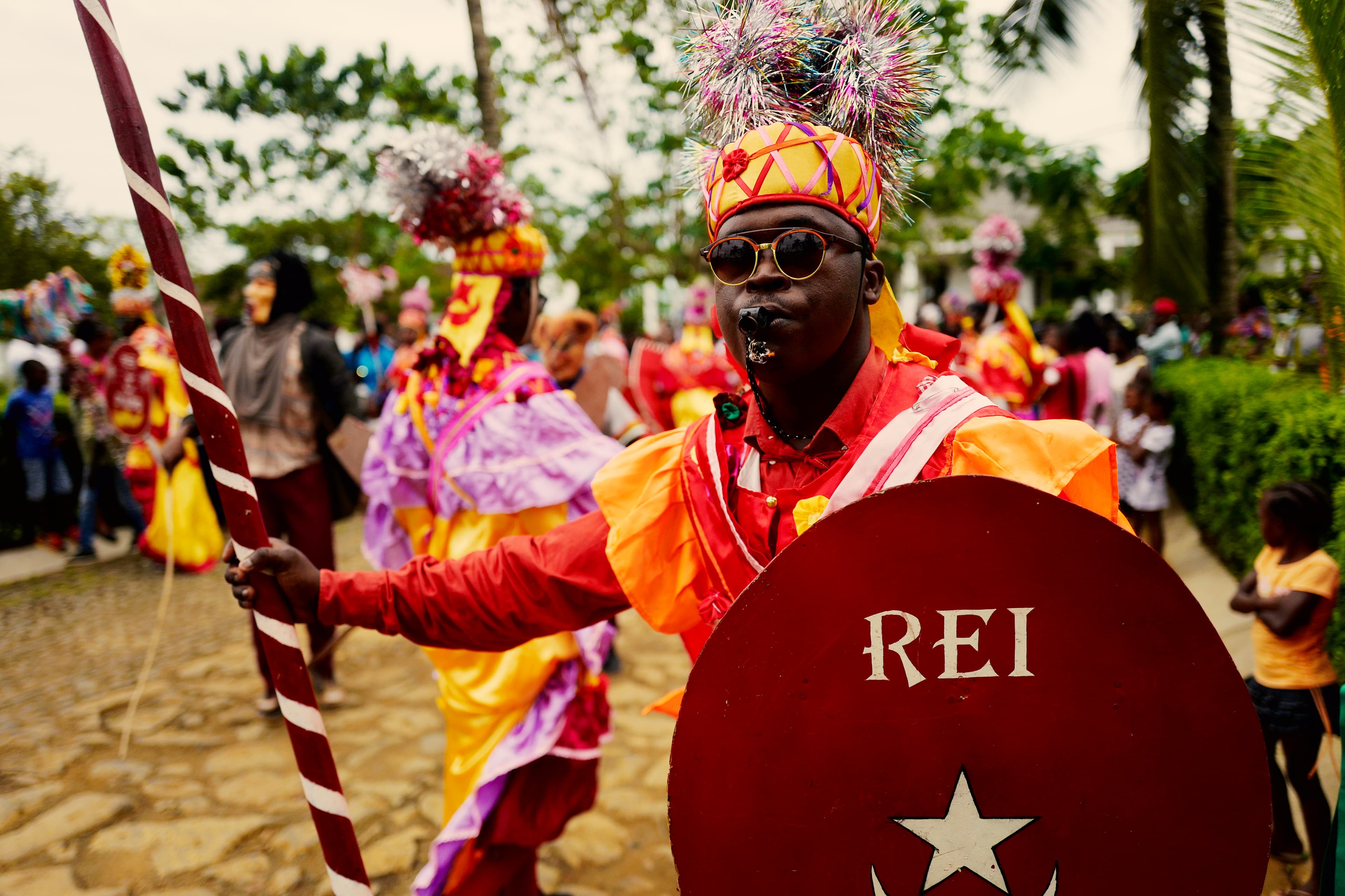 A man in traditional attire in vibrant orange and red tones, with an elaborate headdress